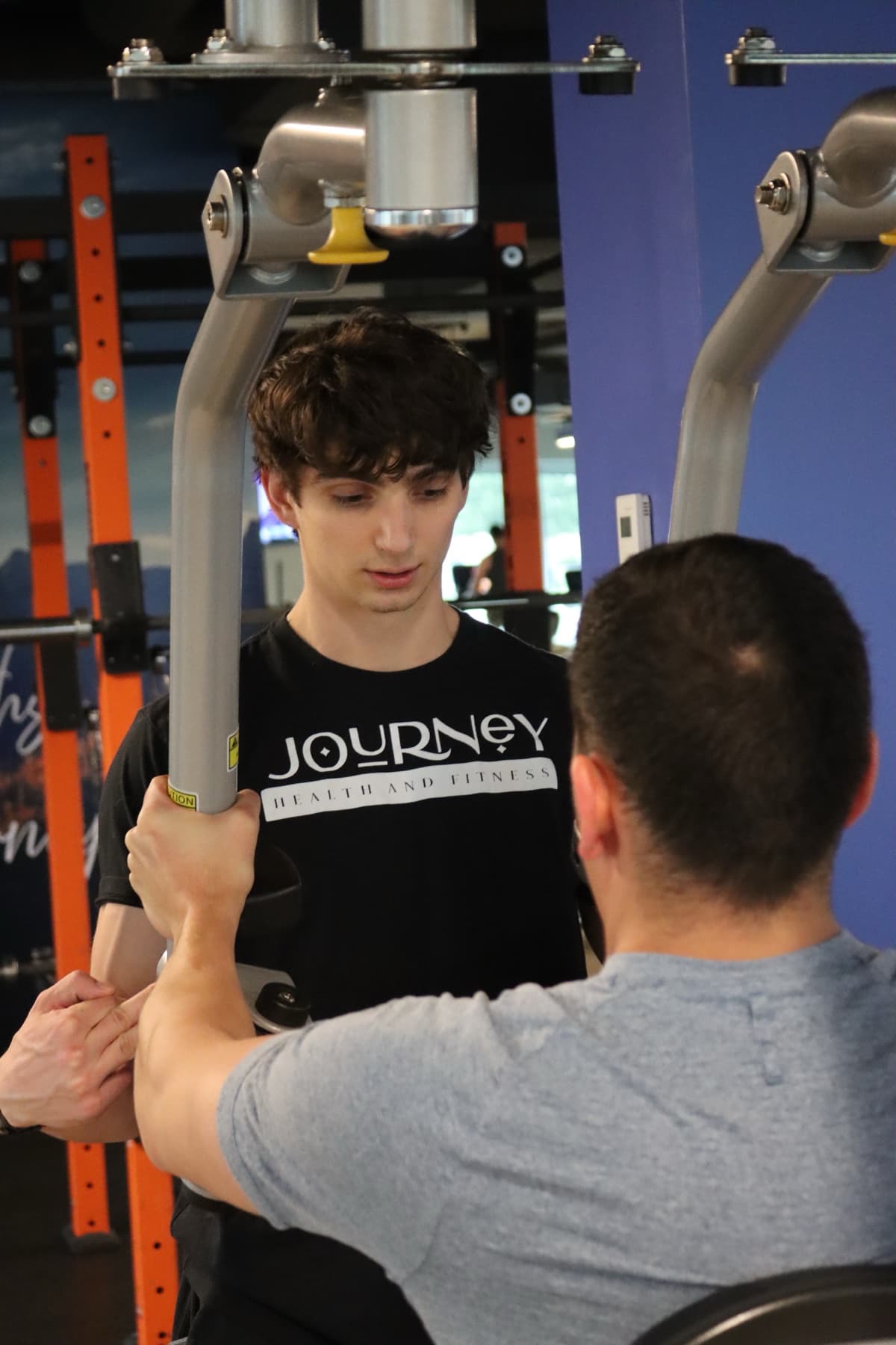 Kris Oddo watching a client use a chest press machine and cueing hand position during a training session
