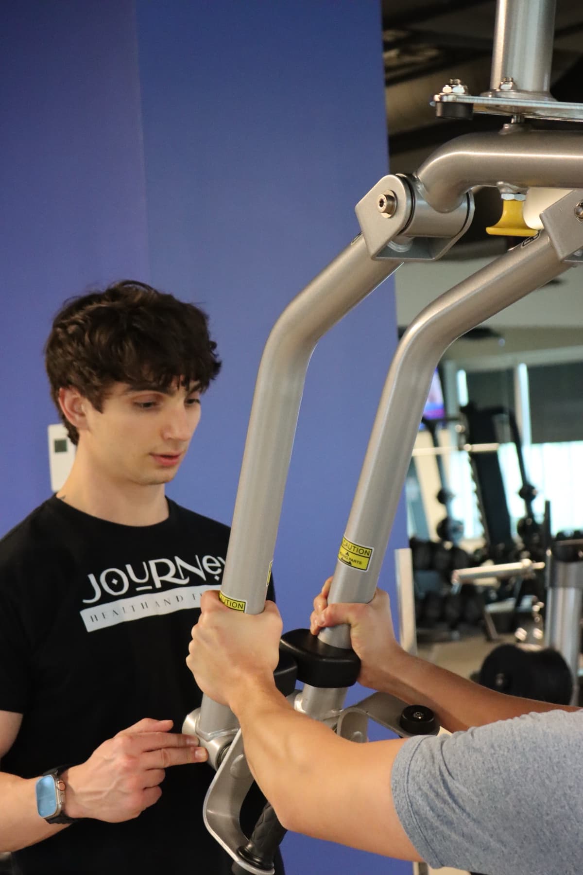Kris Oddo giving a client close form guidance on a gym machine during a coaching session