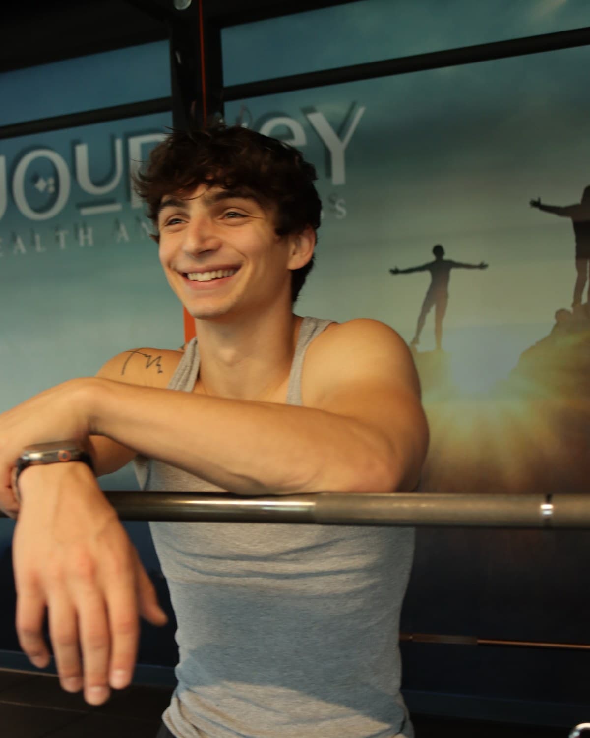 Kris Oddo in the gym, leaning on a barbell and smiling toward the camera