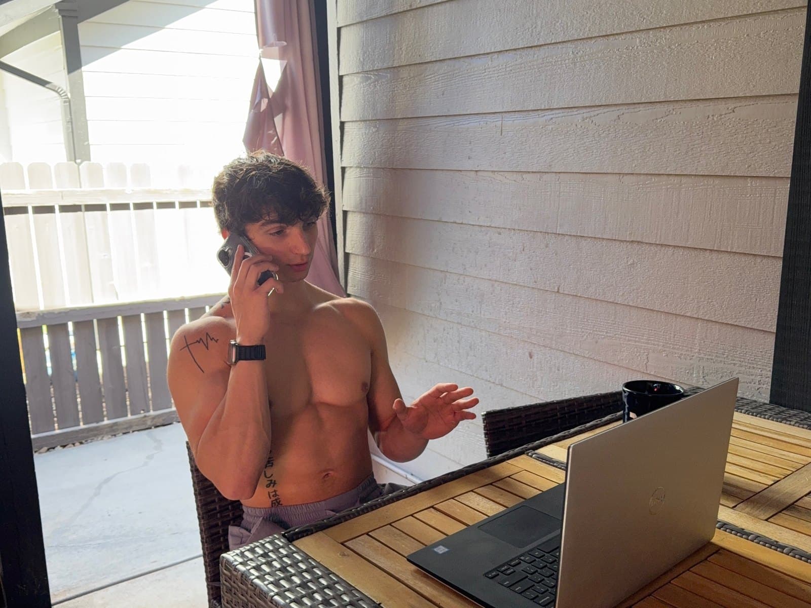 Kris Oddo on his porch, on the phone with a client and talking with his hand, laptop open on the table